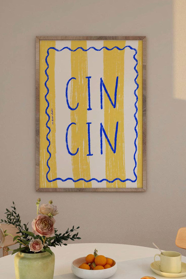 Framed artwork with 'CIN CIN' text above a dining table with a vase, fruit bowl, and bread.