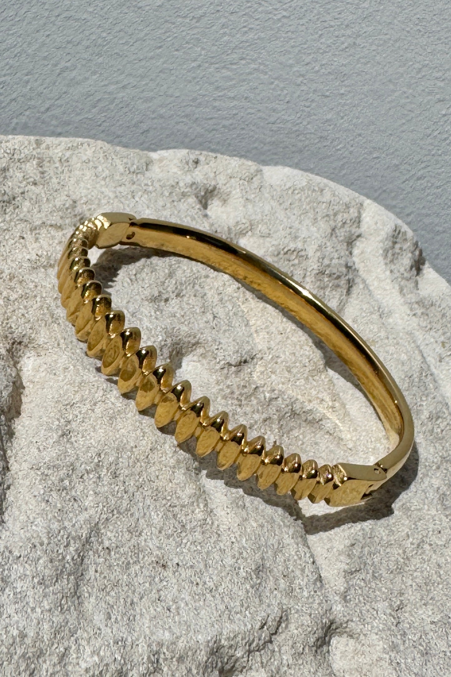 Gold bracelet on a textured stone surface with a gray background