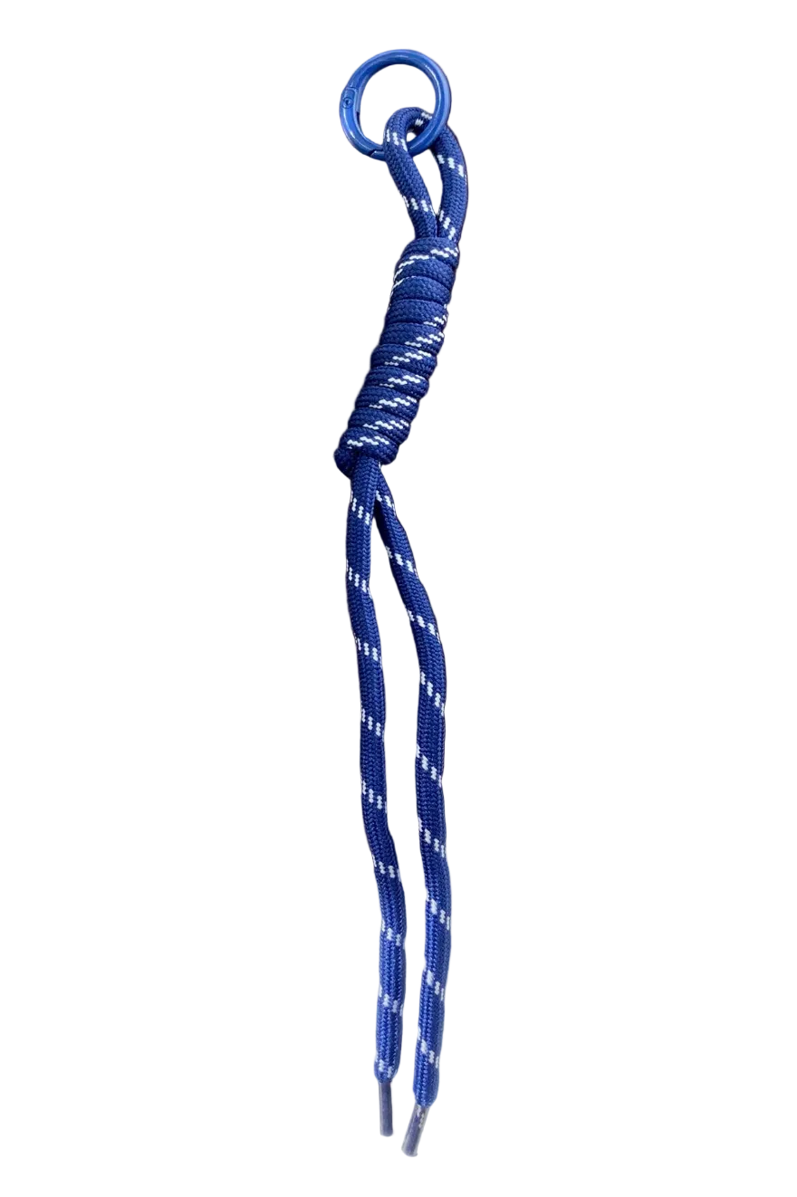 A blue and white patterned paracord keychain or bag charm with a blue metal ring, resting on a dark brown wooden tray.