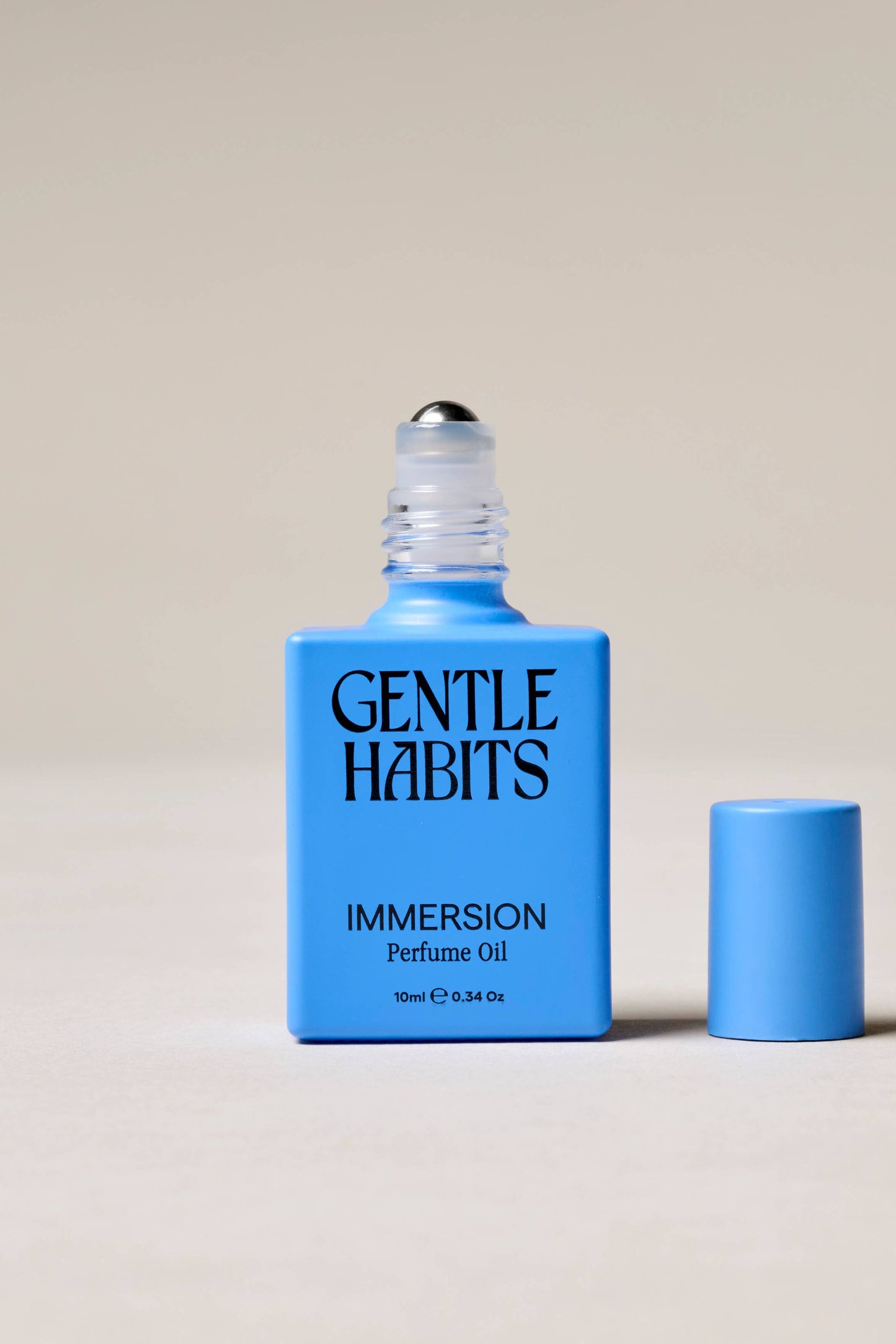 Blue bottle of 'Gentle Habits Immersion' perfume oil on a beige background