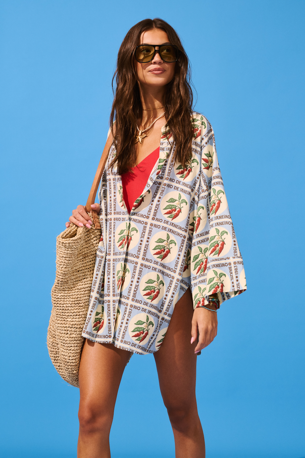 Woman wearing a patterned cover-up and sunglasses against a blue background