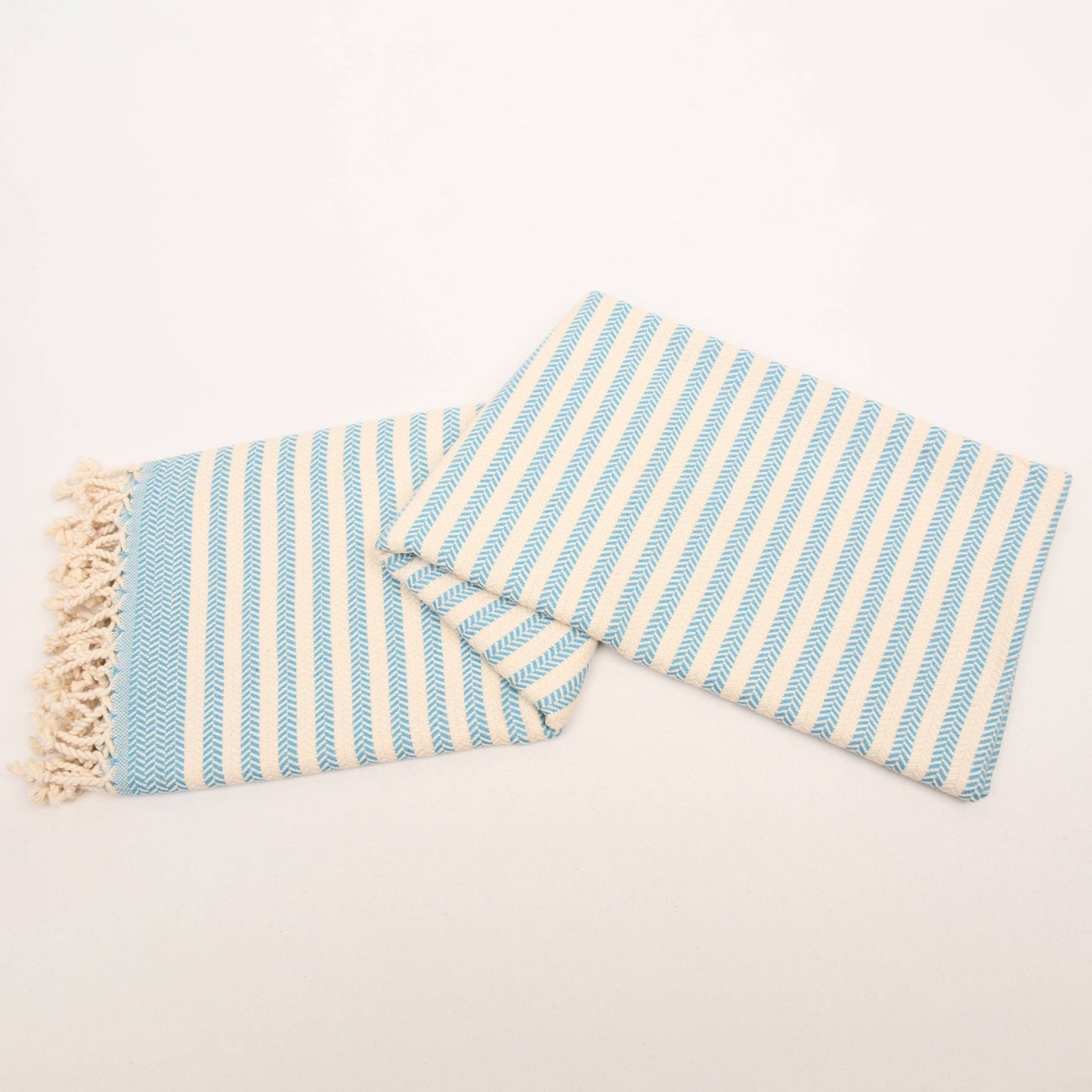 Striped towel with blue and white stripes and tassels on a light gray background