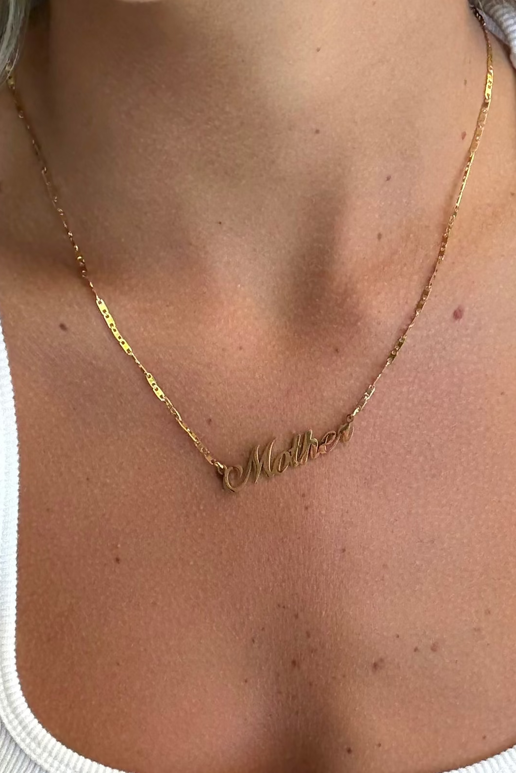 Gold necklace with 'Mother' on a person wearing a white top