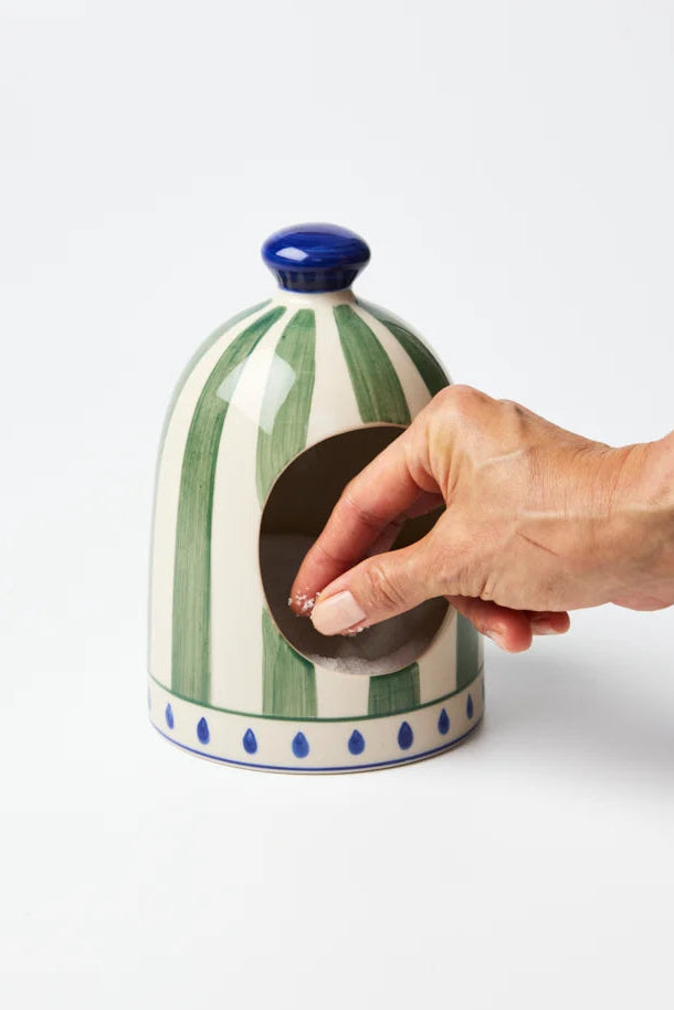 Ceramic jar with green and white striped design and blue accents, being opened by a hand on a white background.