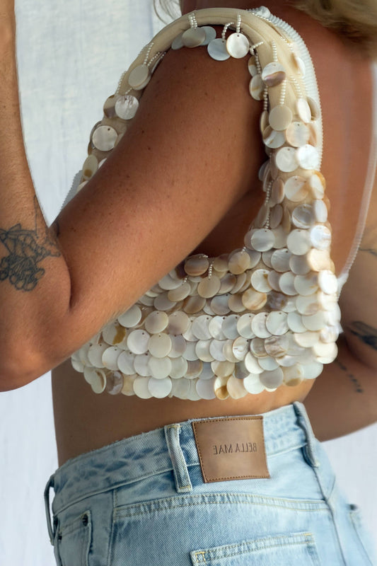 Person wearing a beaded top and denim jeans with a plain background
