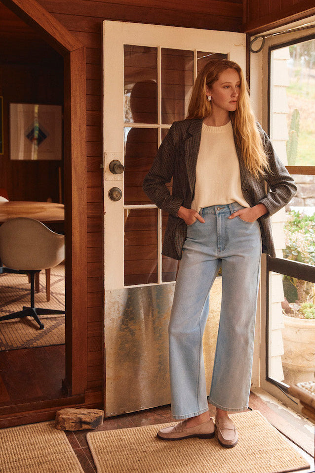 Woman standing in a wooden interior space with large windows.