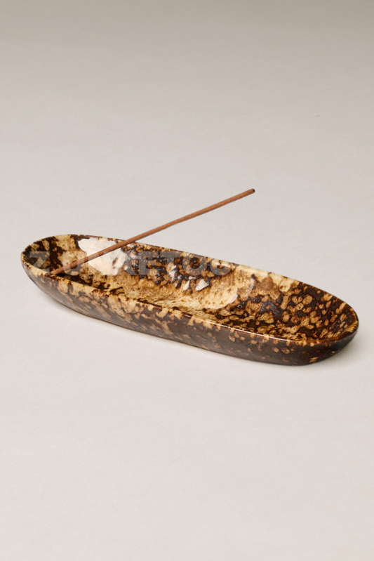 Decorative ceramic oval dish with an incense stick on a beige background
