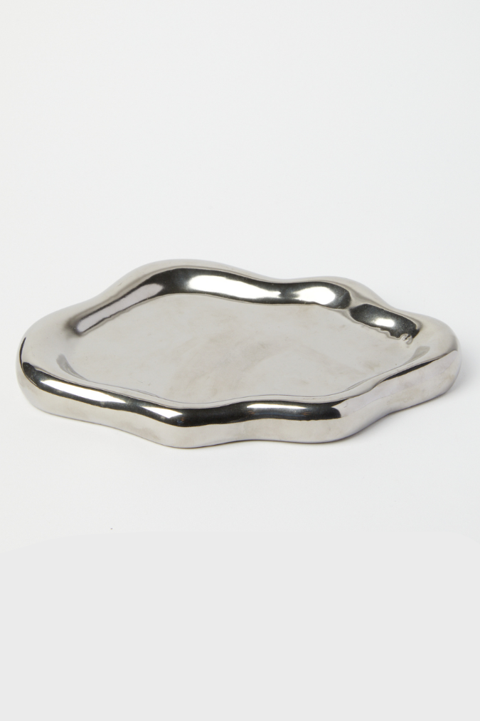 A small, irregularly shaped metallic silver tray with a polished, wavy edge, photographed on a seamless white background.