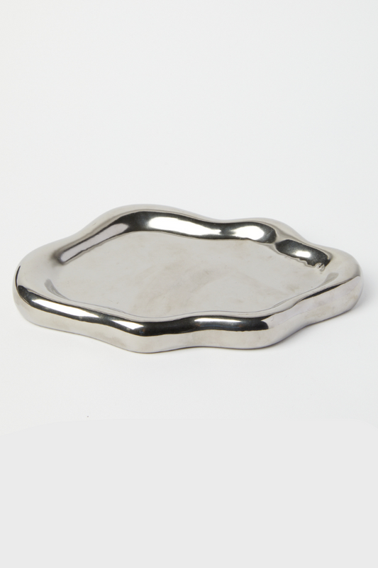 A small, irregularly shaped metallic silver tray with a polished, wavy edge, photographed on a seamless white background.