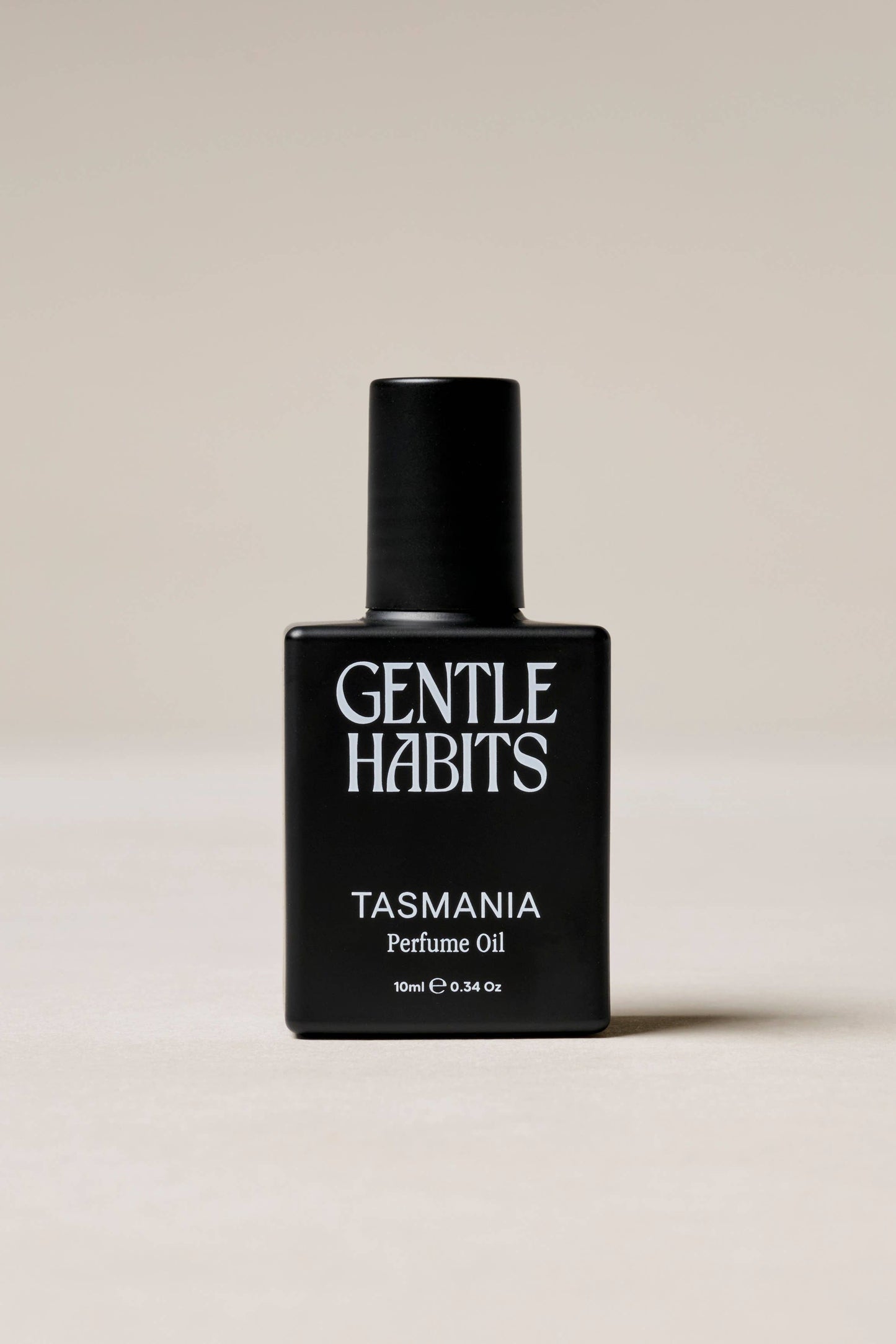 Black perfume bottle labeled 'Gentle Habits Tasmania' on a beige background