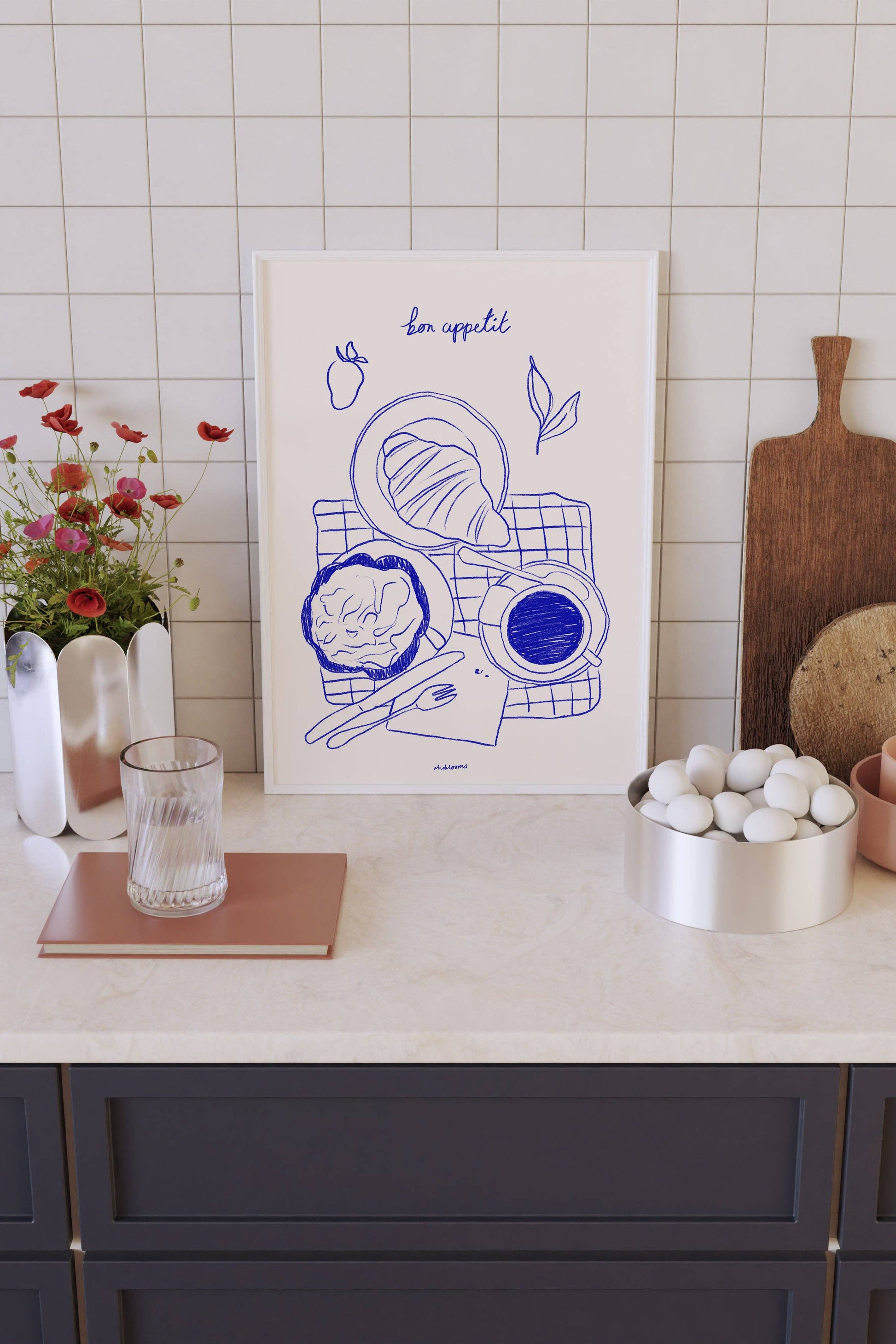 Kitchen counter with a framed artwork, cutting board, and decorative items against a tiled wall.