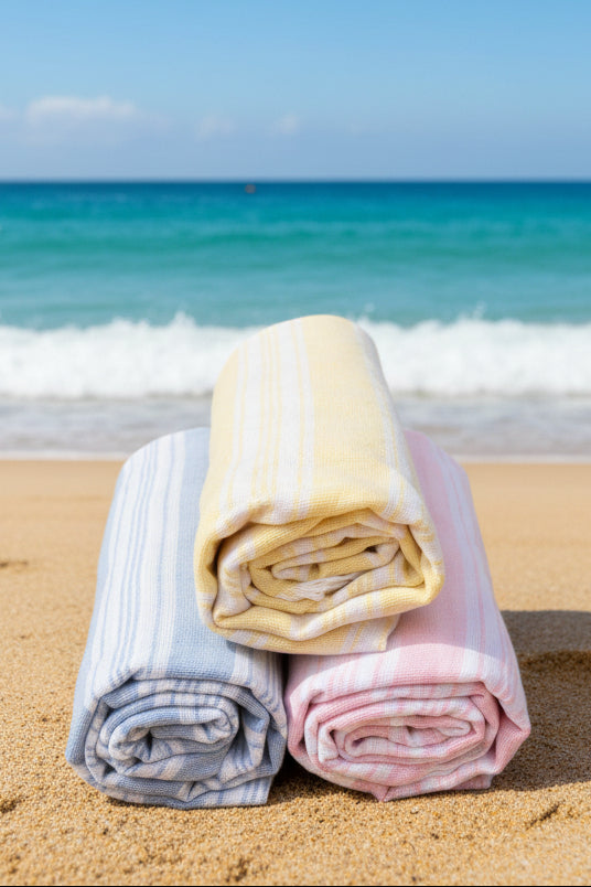 Three folded towels in pastel colors on a beach