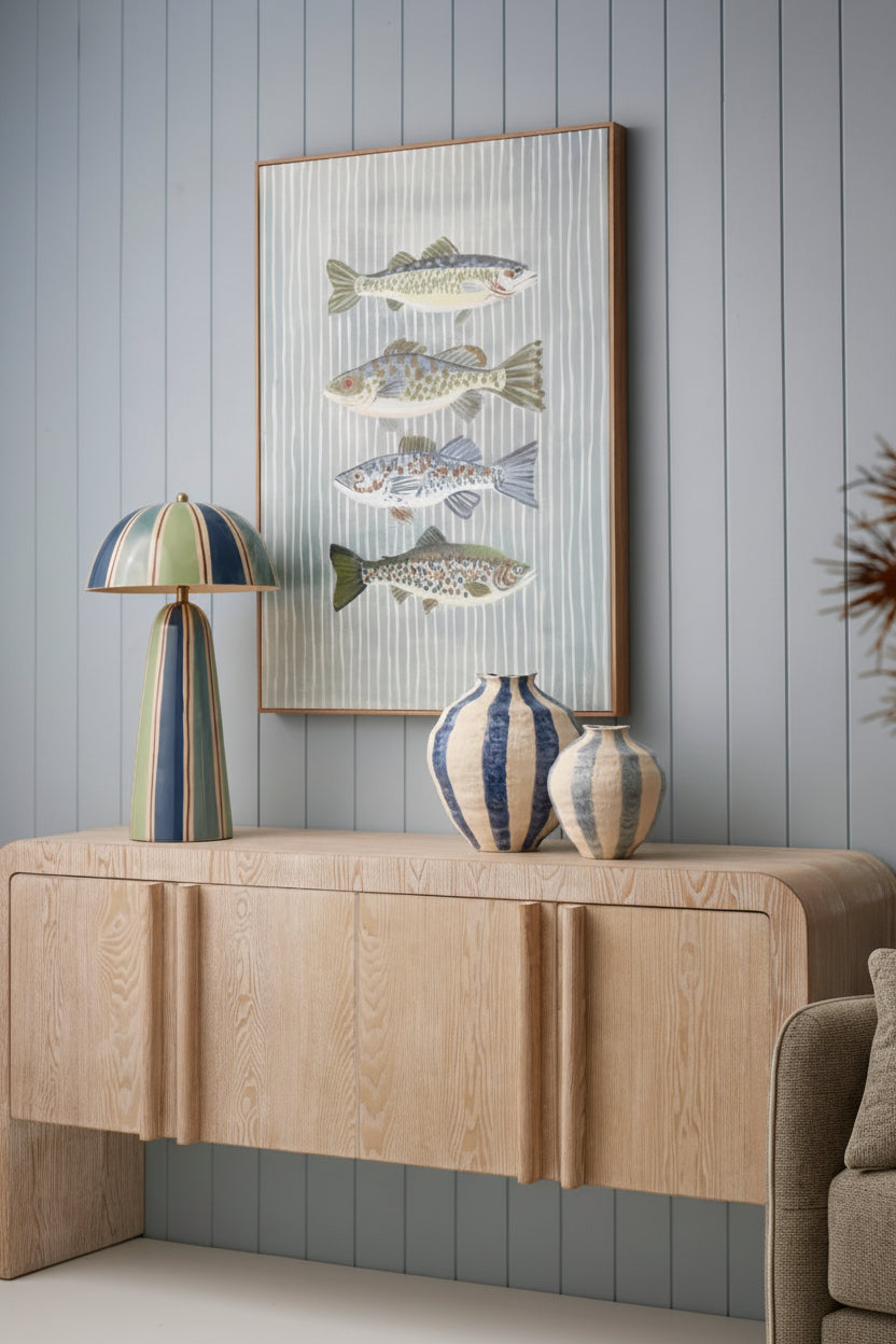 Living room interior with a wooden console table, lamp, and framed fish artwork on a gray paneled wall.