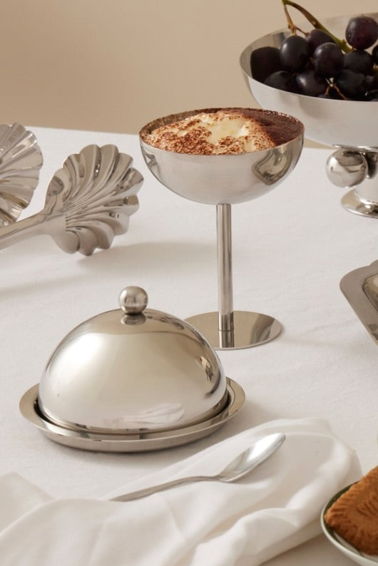 Table setting with silver platters, a cup of coffee, and dessert on a white tablecloth.