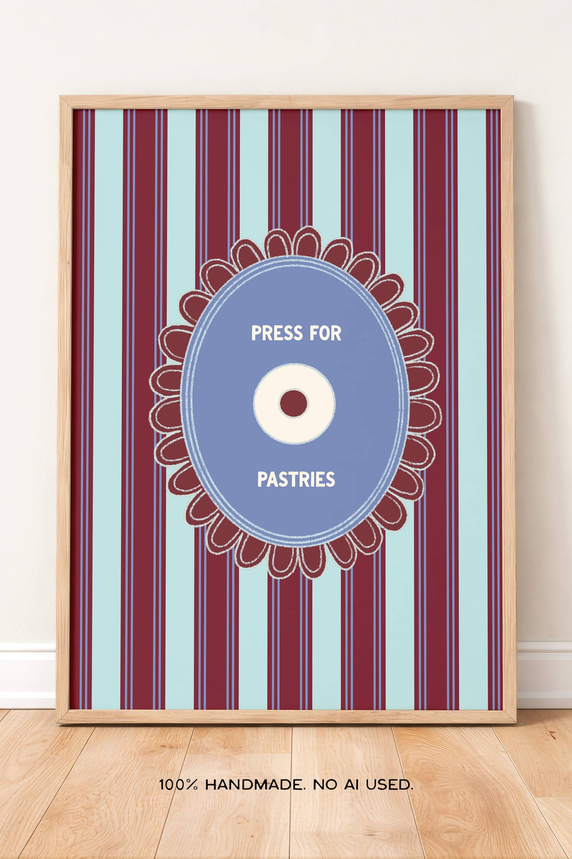 A framed vertical art print with a striped pattern in burgundy, light blue, and white, featuring a central blue oval with a pastry illustration and the words 'PRESS FOR PASTRIES.' The print is leaning against a white wall on a light wood floor.