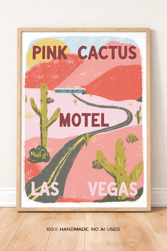 A framed art print featuring a retro-style illustration of the Pink Cactus Motel in Las Vegas, displayed leaning against a white wall on a light wood floor.
