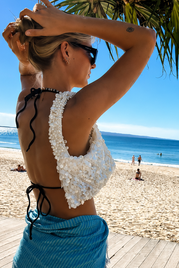 Woman in a white top and blue sarong on a beach with ocean and sky in the background