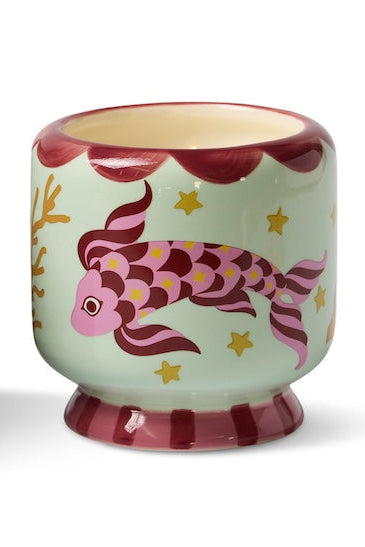 Decorative candle with fish design next to its packaging on a white background