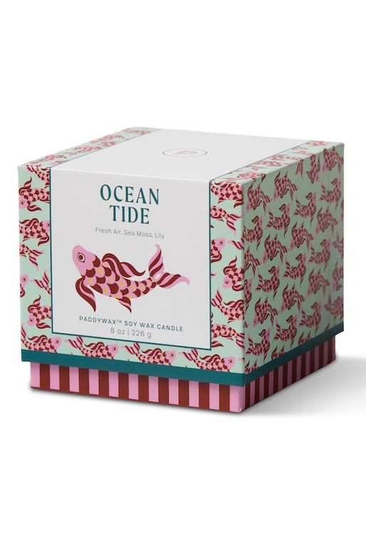 Decorative candle with fish design next to its packaging on a white background