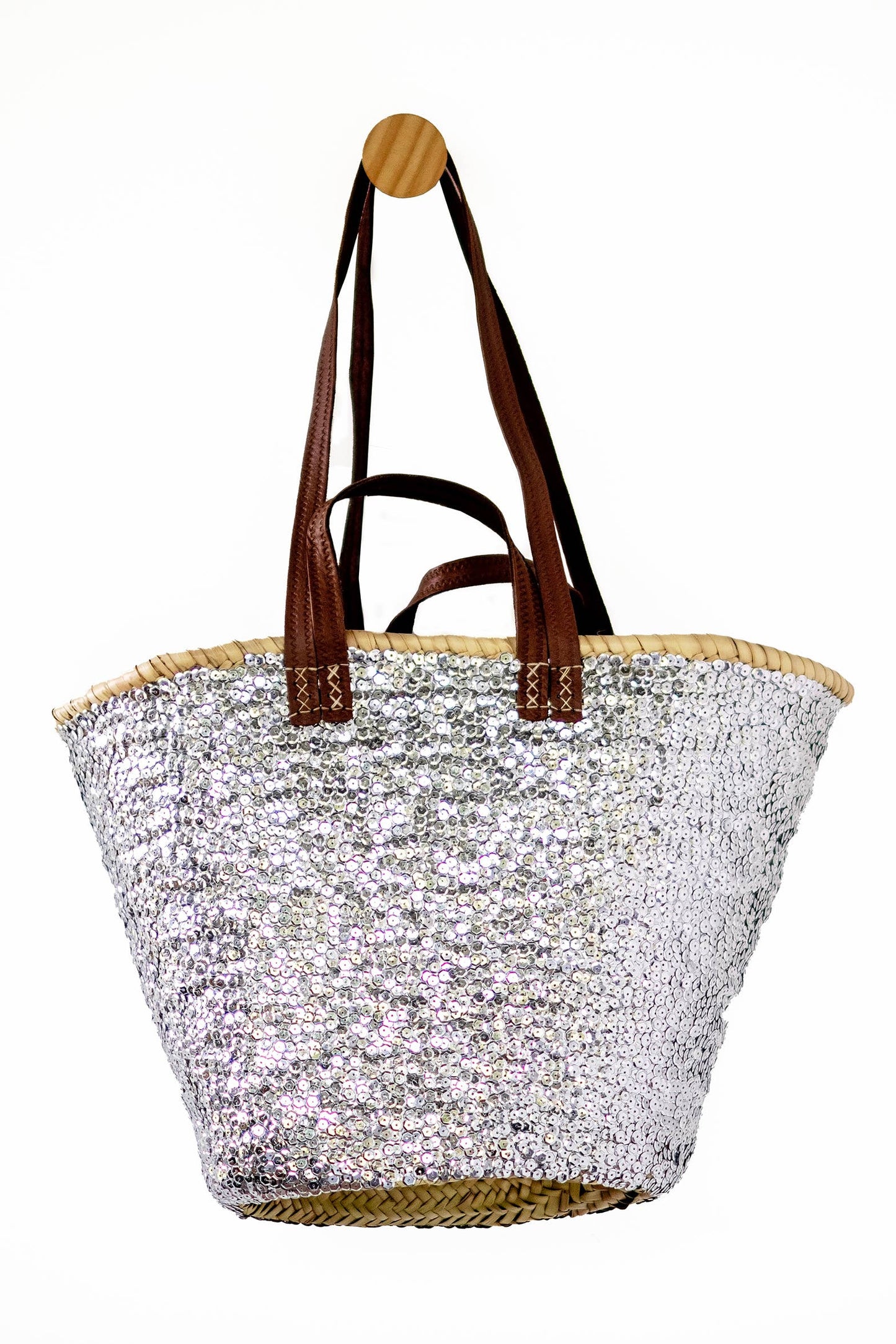 A silver sequined beach tote bag with brown leather shoulder straps and a natural woven straw trim, shown against a plain white background.
