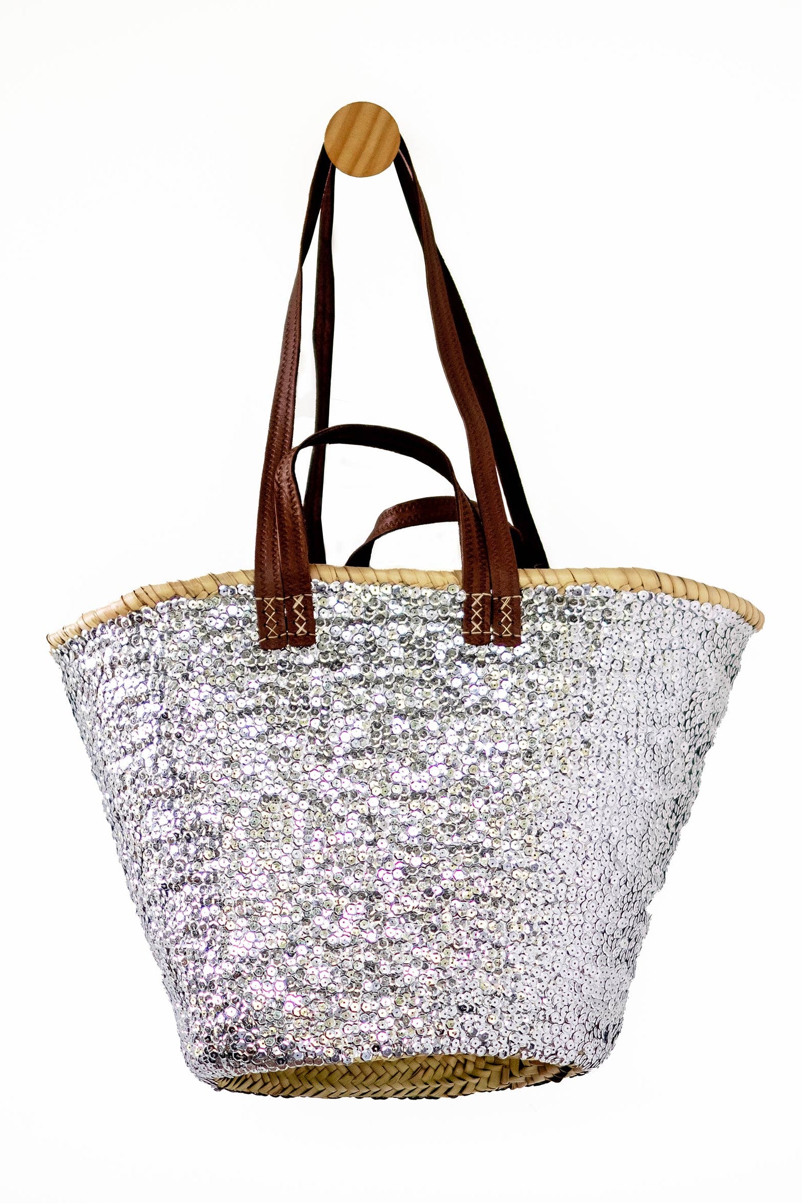 A silver sequined beach tote bag with brown leather shoulder straps and a natural woven straw trim, shown against a plain white background.