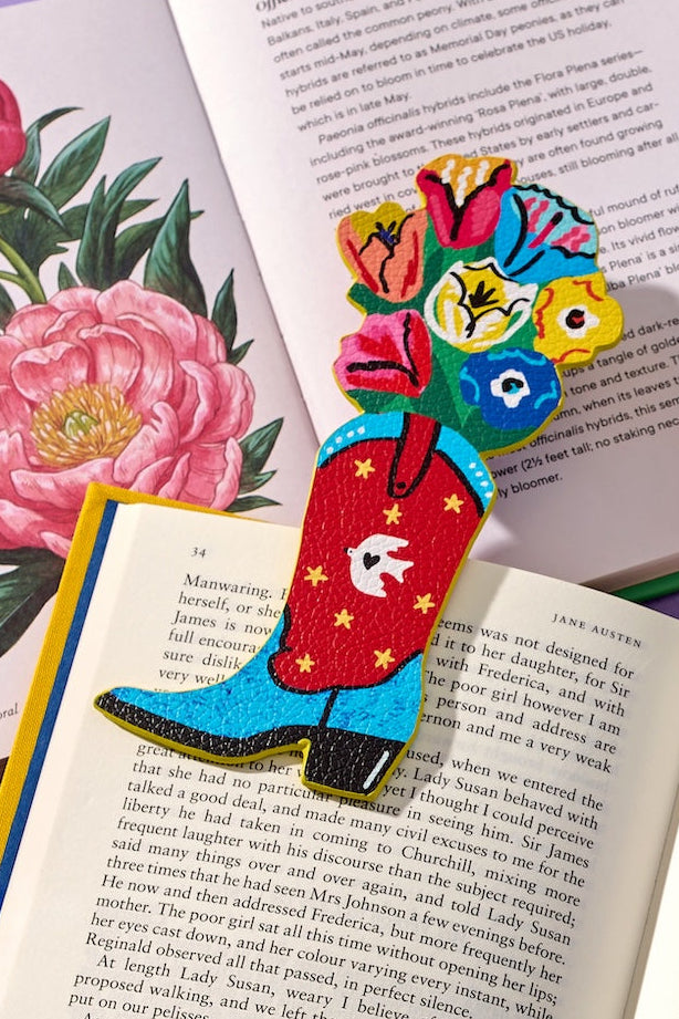 A colorful book bookmark shaped like a red stocking with yellow stars and a floral bouquet on top, resting on an open book next to a peony illustration.