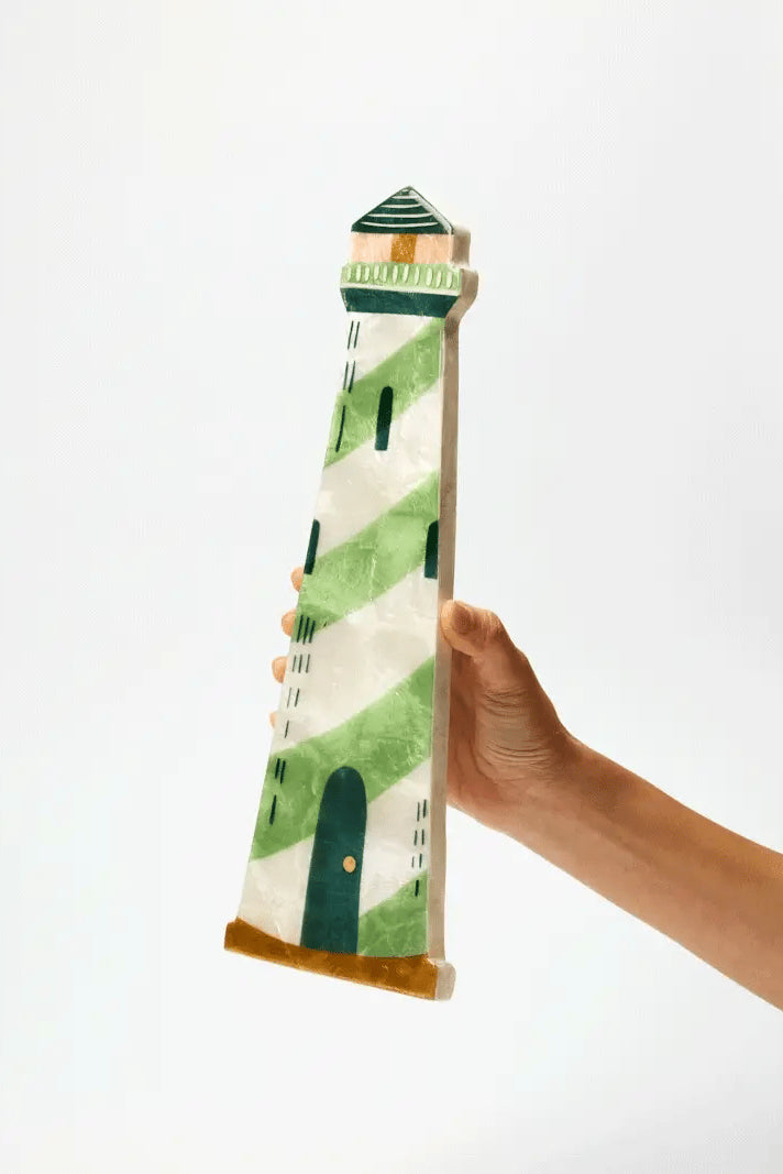 Hand holding a decorative item shaped like a lighthouse with green and white pattern on a white background