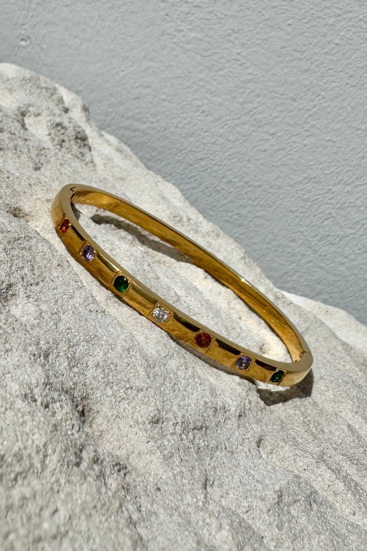 Gold bracelet with embedded gemstones on a textured surface