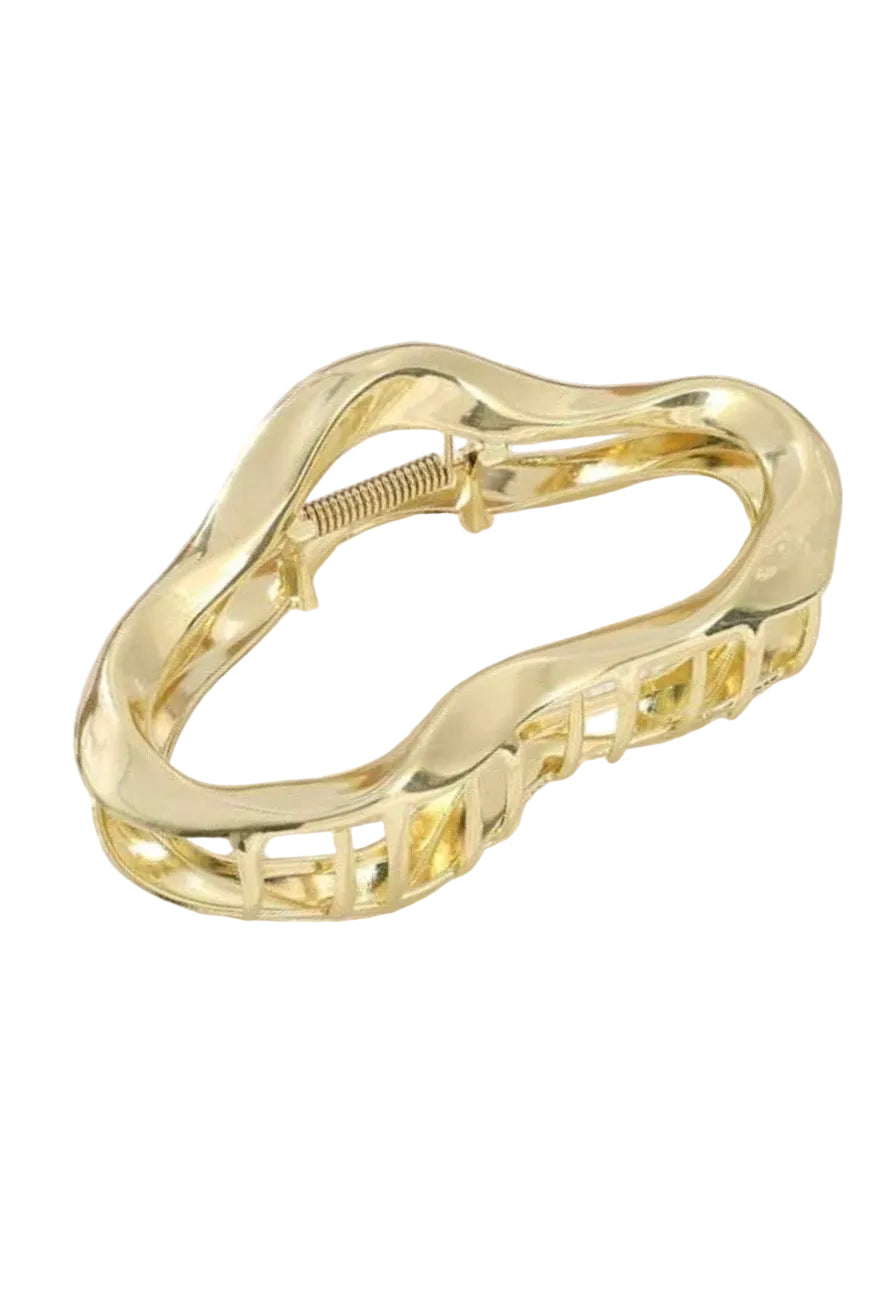 Gold hair clip on a white surface with a wooden frame in the background