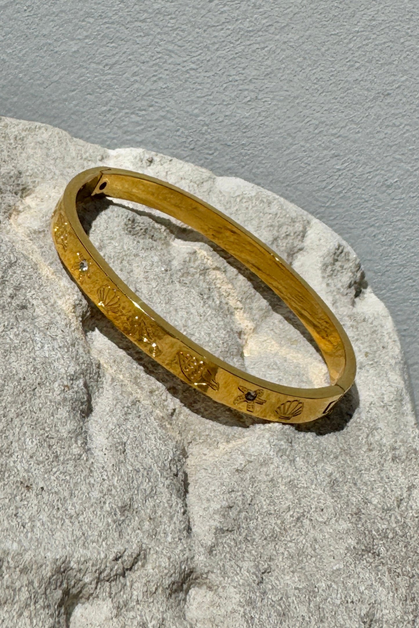 Gold bracelet with engraved design on a textured stone surface