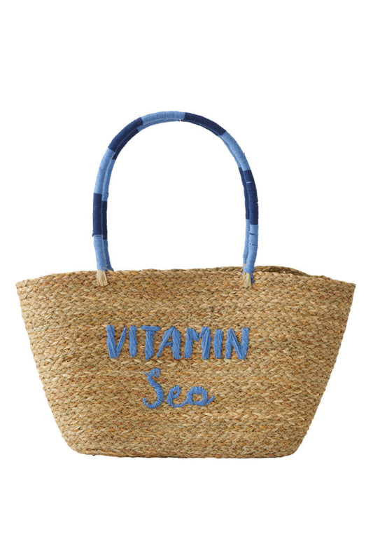 A natural straw tote bag with blue embroidered text reading 'VITAMIN Sea' on the front and a blue-and-navy patchwork woven handle, shown on a plain white background.