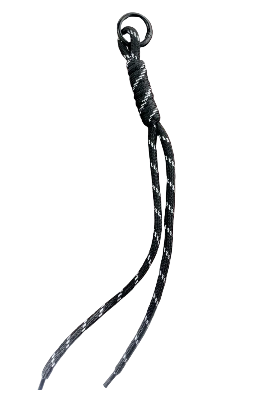 A black braided rope keychain or lanyard with a black metal ring, resting on a dark brown wooden tray.
