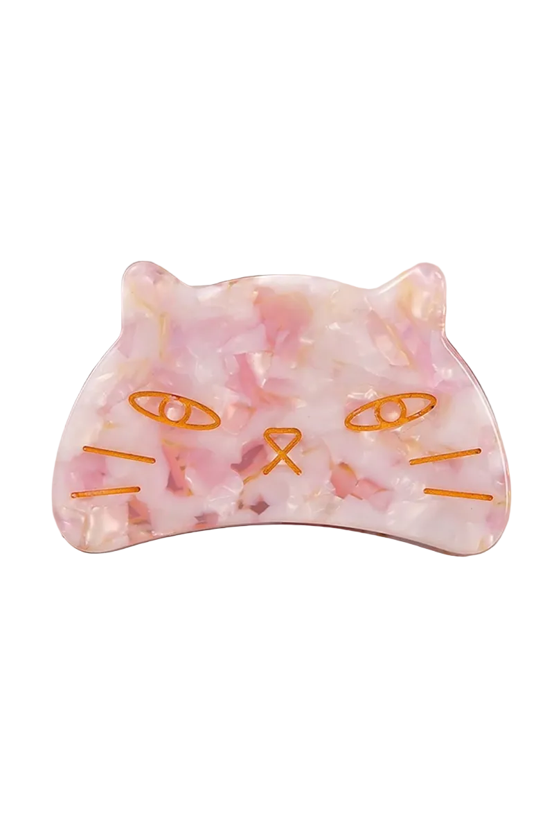 A cat-shaped hair claw clip with a pink and white marbled pattern and orange embroidered facial features, resting on a beige tray.