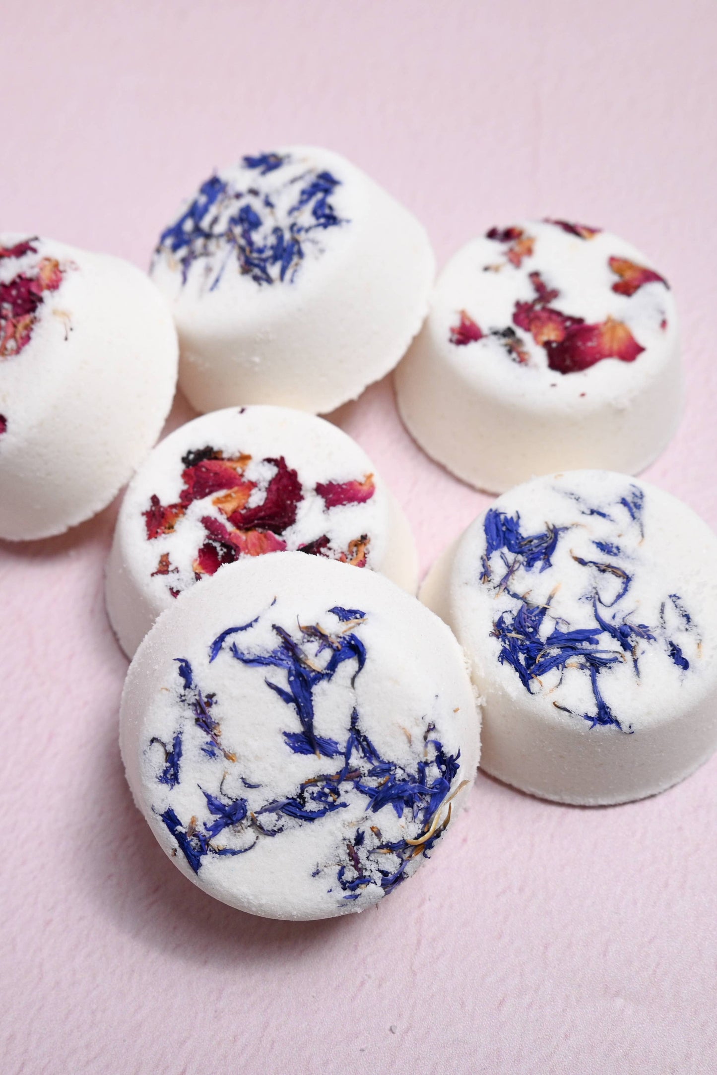 White bath bombs with floral toppings on a pink background