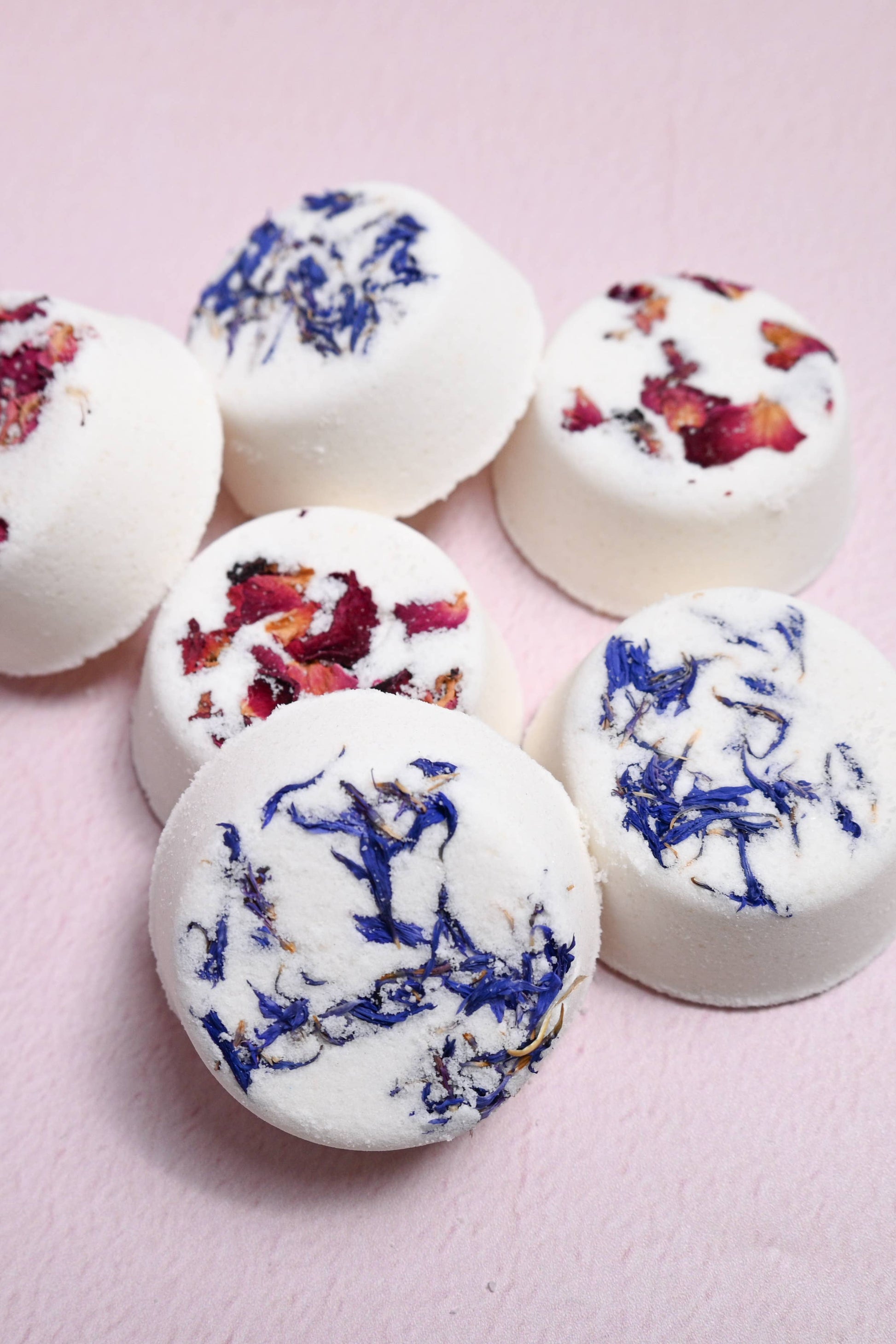 White bath bombs with floral toppings on a pink background
