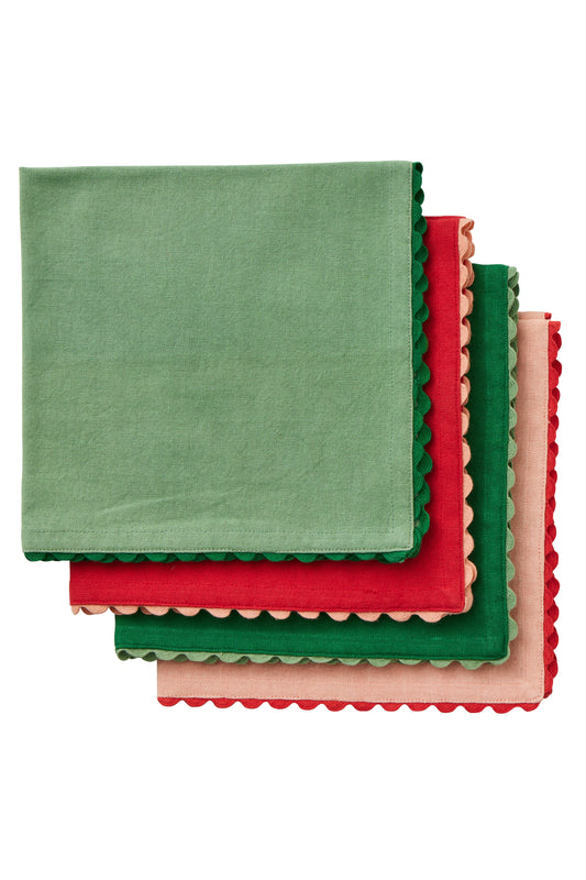 Four square fabric napkins with scalloped edges stacked in an overlapping fan arrangement. The napkins are sage green, red, forest green, and light pink, shown against a plain white background.