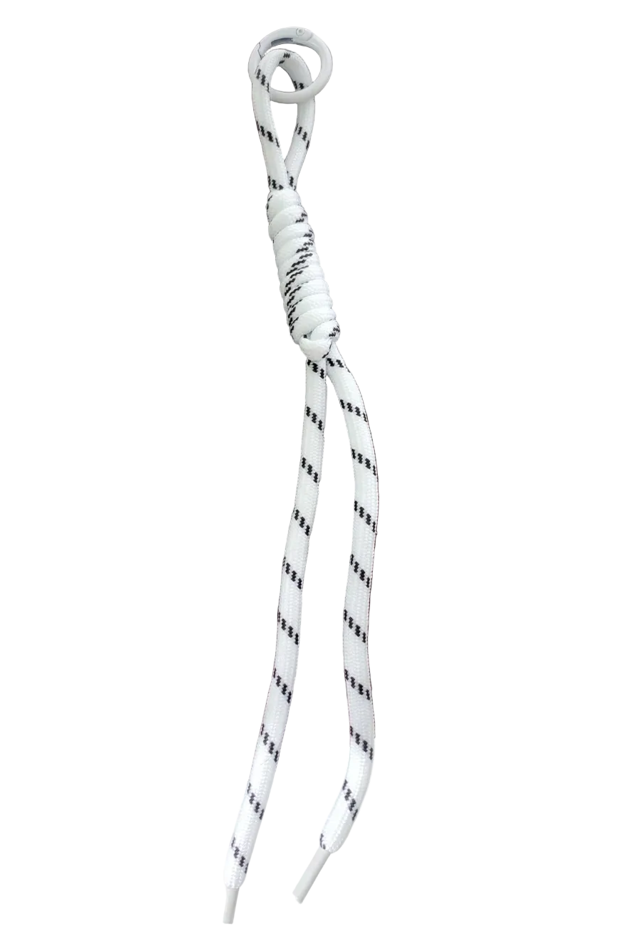 A white braided shoelace with a black dotted pattern and a metal eyelet, laid diagonally on a dark brown wooden tray.