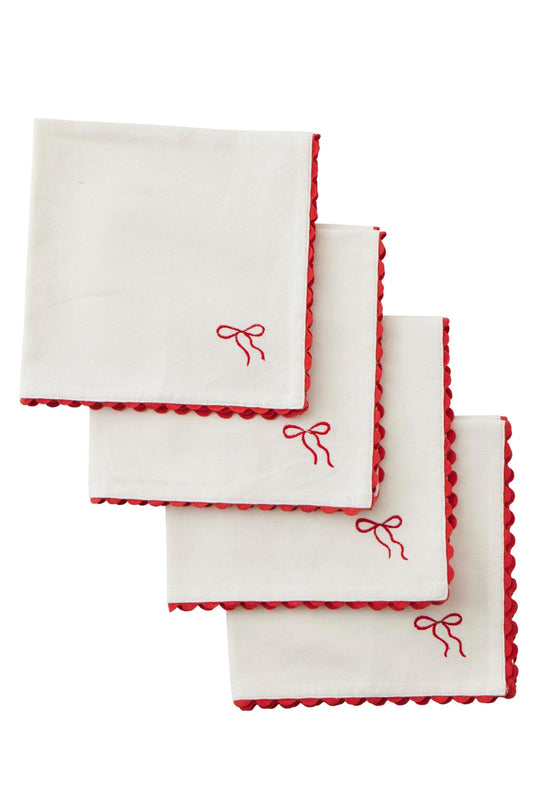 Four white square napkins with red scalloped edges and a small red embroidered bow near one corner, arranged in a staggered stack on a white background.