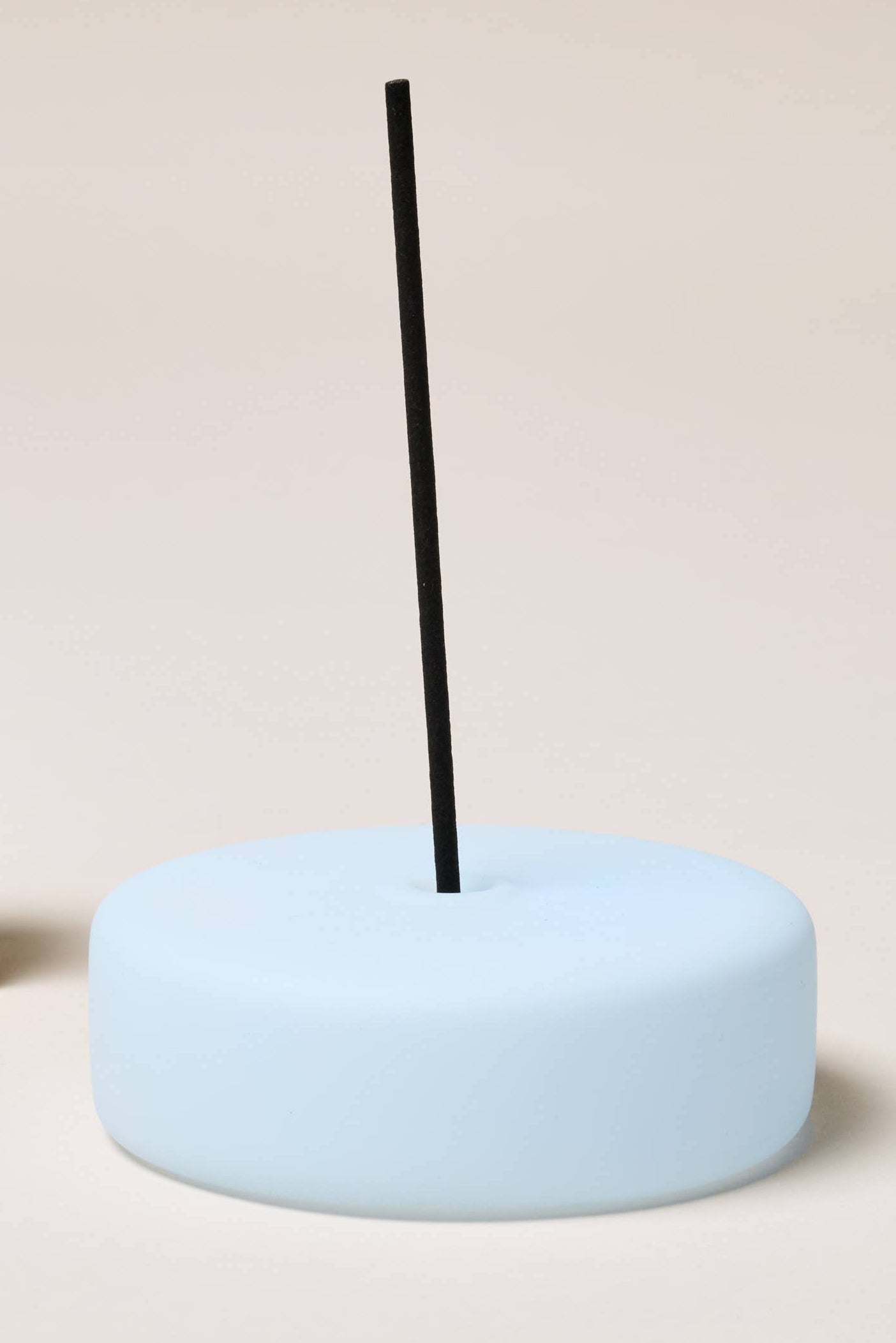 Light blue incense holder with a black incense stick on a beige background.