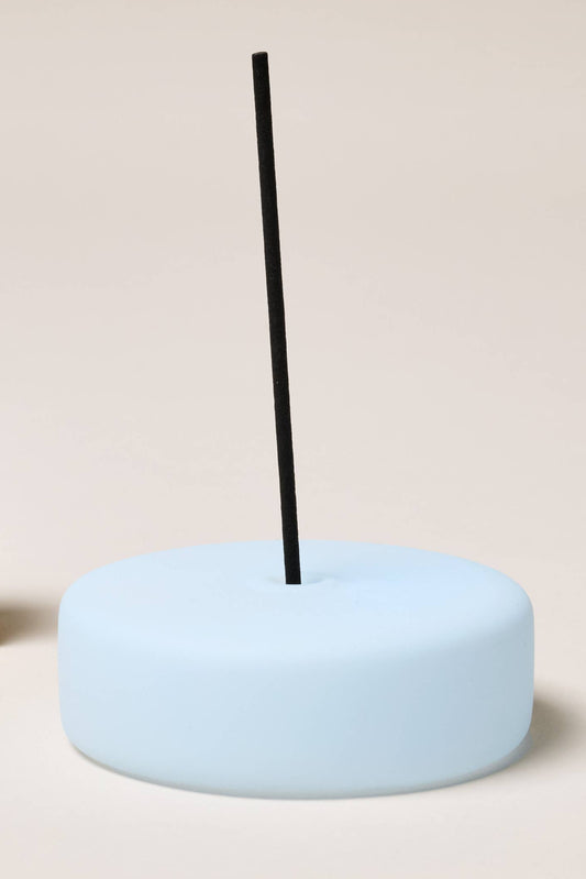 Light blue incense holder with a black incense stick on a beige background.