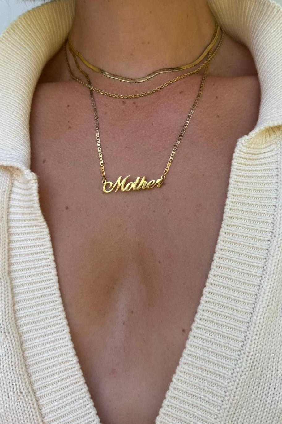 Gold 'Mother' necklace worn by a person with a light-colored sweater.