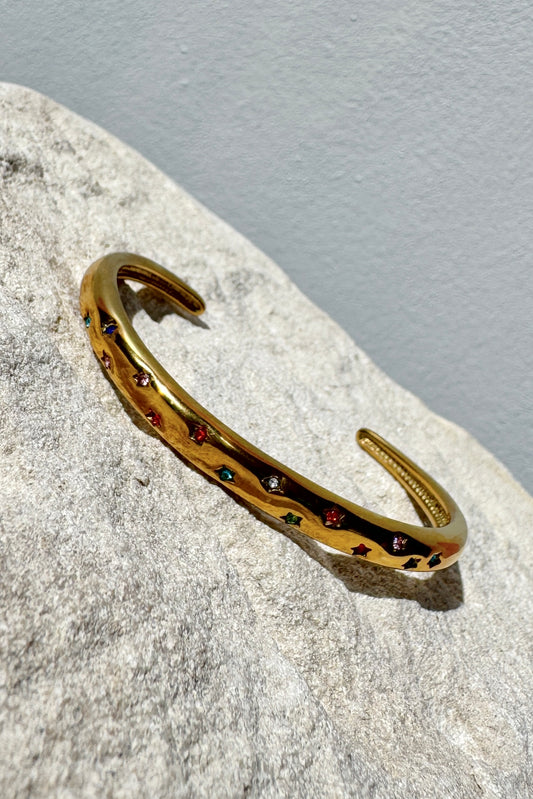 Gold bracelet with embedded stones on a textured stone surface