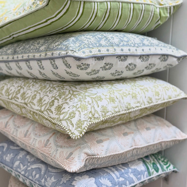 Stack of patterned cushions in various colors against a white wall.