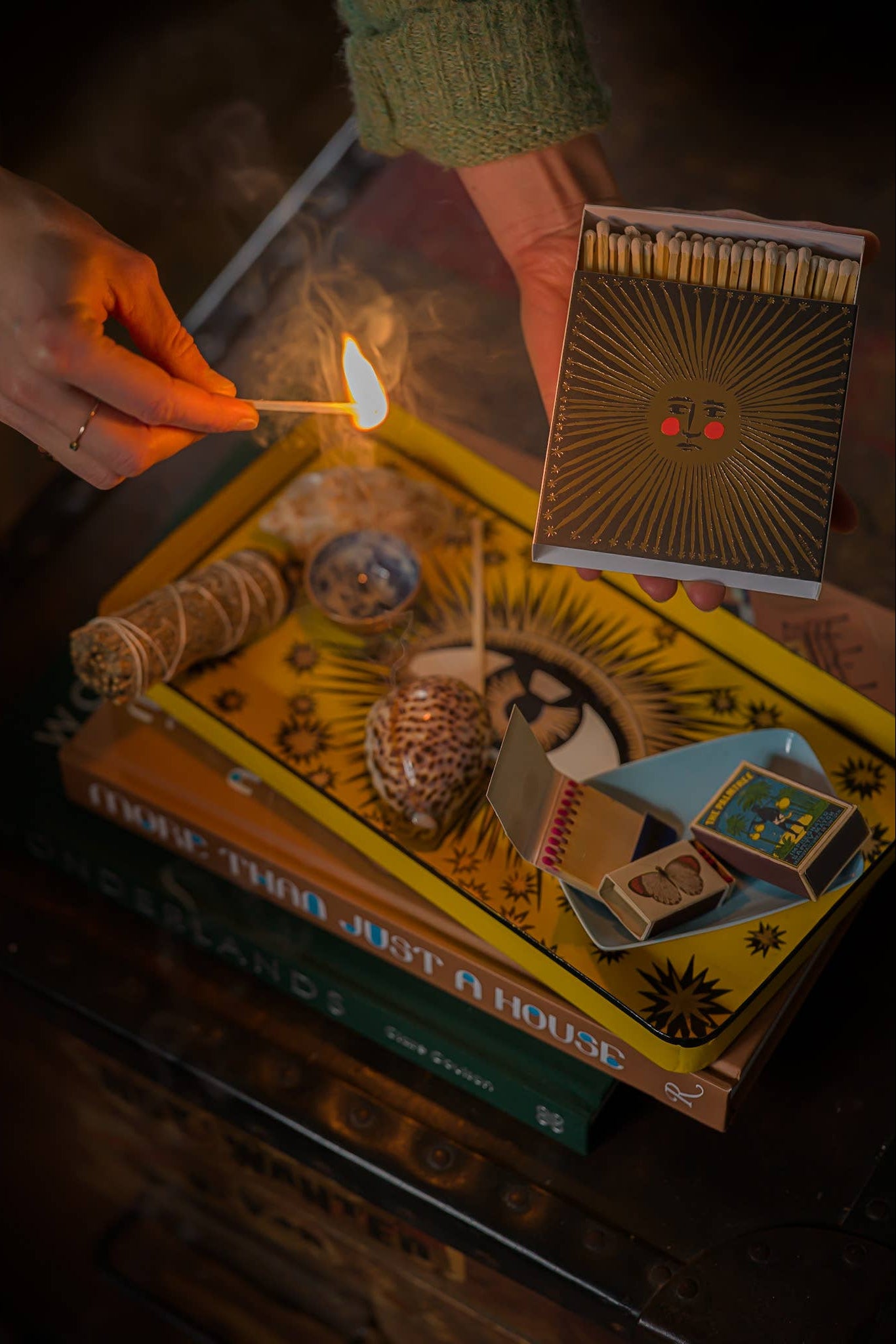 Person lighting a match over a stack of books with a matchbox on top.