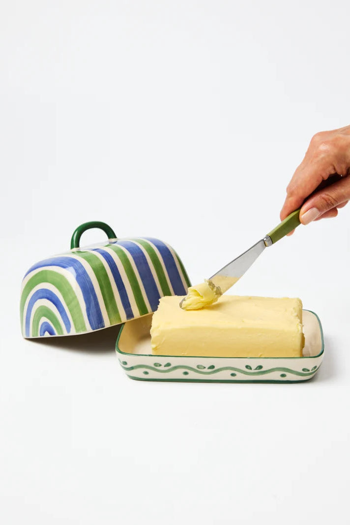 Butter dish with striped lid and a hand spreading butter on a knife.