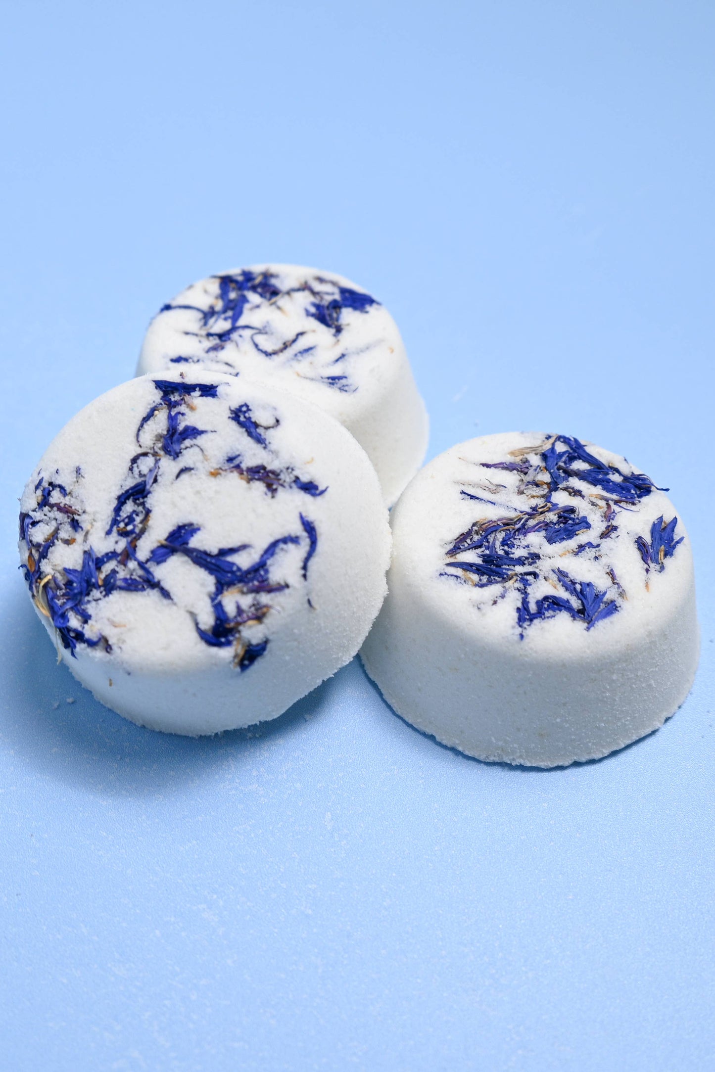 Three white bath bombs with blue swirls on a light blue background