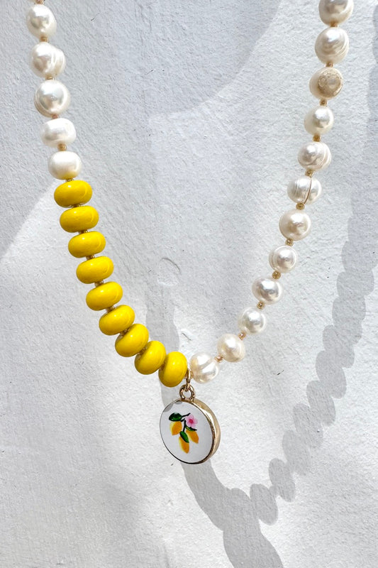 Necklace with yellow beads and a lemon pendant on a light gray background