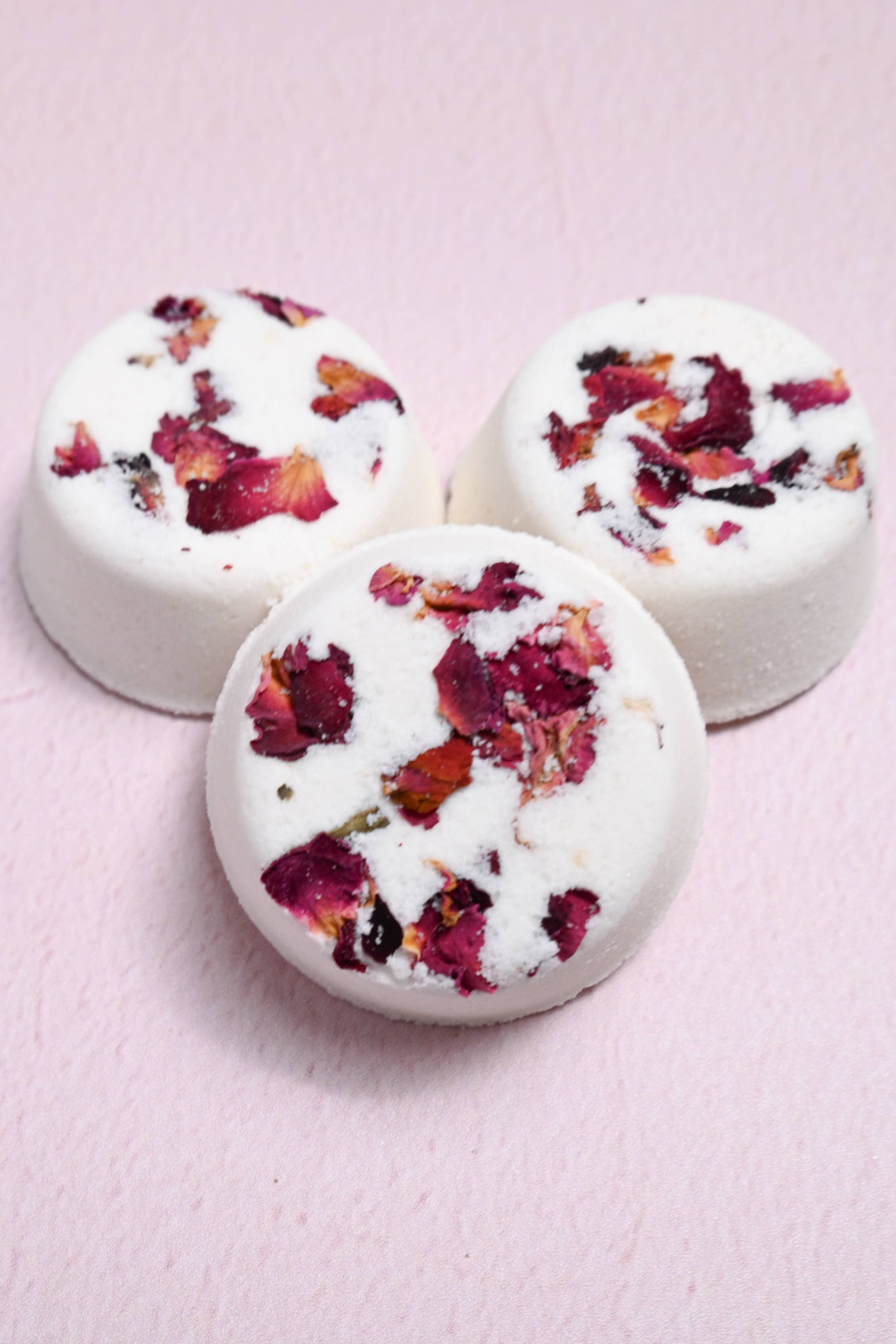 Three round white treats with dried flowers on a pink background